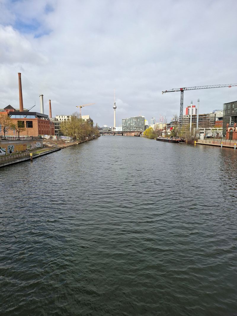 Blick über die Spree in Berlin mit dem Fernsehturm im Hintergrund an einem leicht bewölkten Tag.