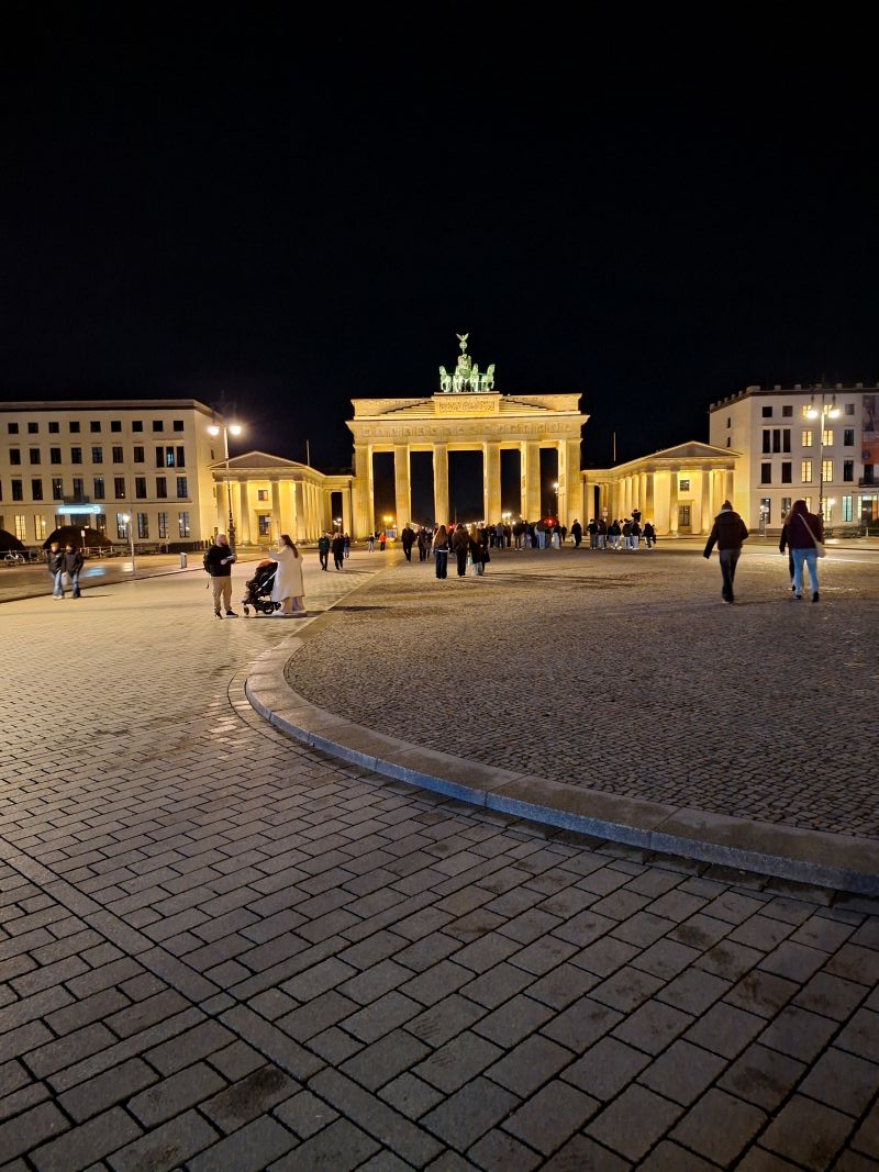 Das hell erleuchtete Brandenburger Tor in Berlin bei Nacht mit Fußgängern auf dem davorliegenden Platz.