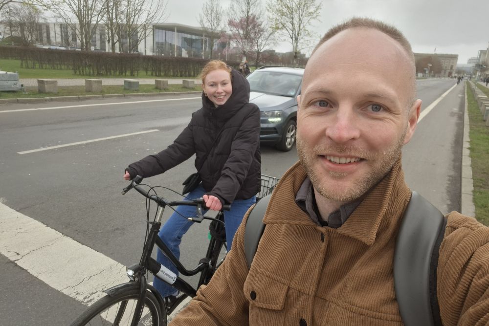 Der Blogger und seine Partnerin auf Fahrrädern auf einer Straße in Berlin, im Hintergrund das Bundeskanzleramt.