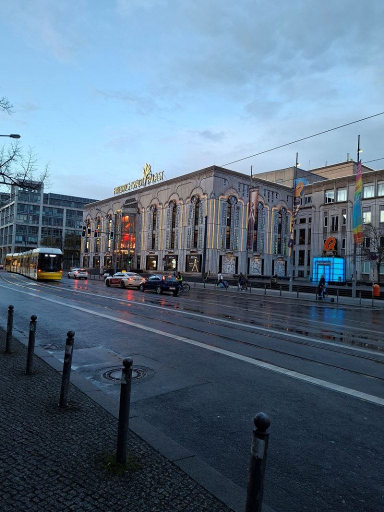 Außenansicht des Friedrichstadt-Palasts in Berlin an einem regnerischen Abend mit Spiegelungen auf der Straße.