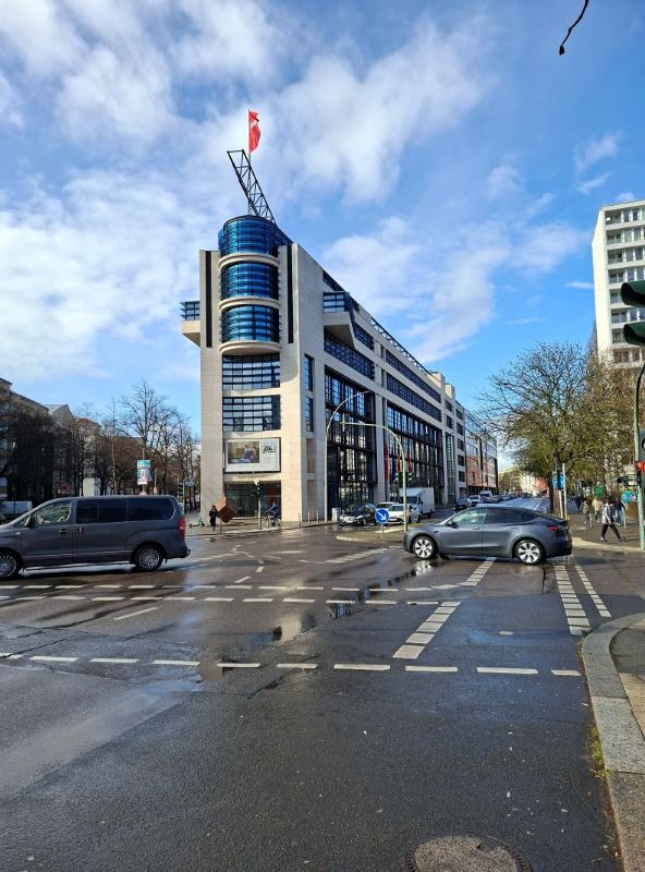Das markante, keilförmige Gebäude der SPD-Parteizentrale (Willy-Brandt-Haus) an einer nassen Straßenkreuzung in Berlin.