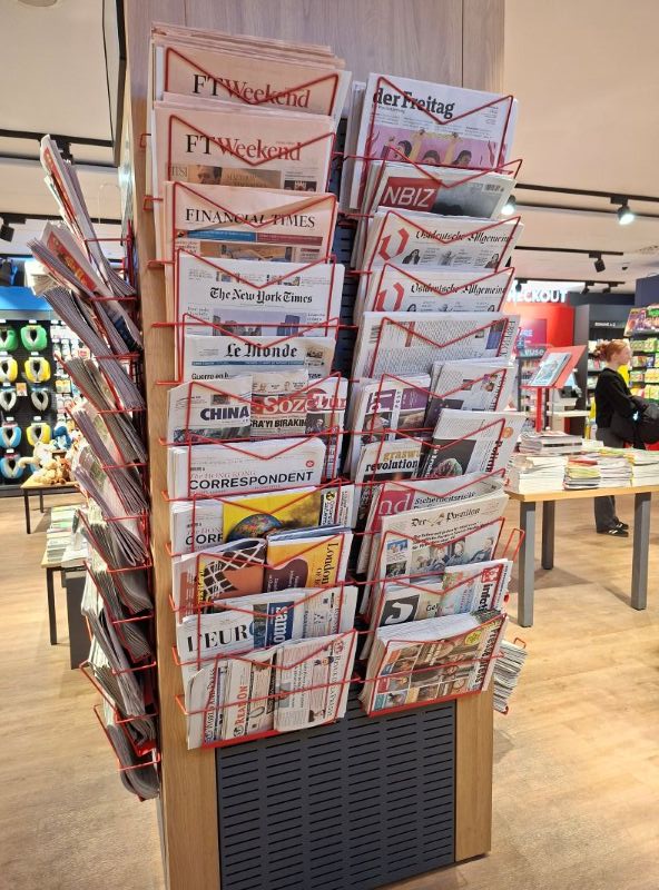 Ein gut gefüllter Zeitschriftenständer in einer Buchhandlung mit verschiedenen internationalen und nationalen Tageszeitungen.