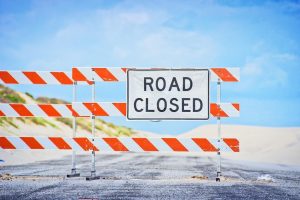 Ein „Road Closed“-Schild auf einer Absperrung vor Sanddünen, das die Grenzen der Kritik am Finanzblog markiert.