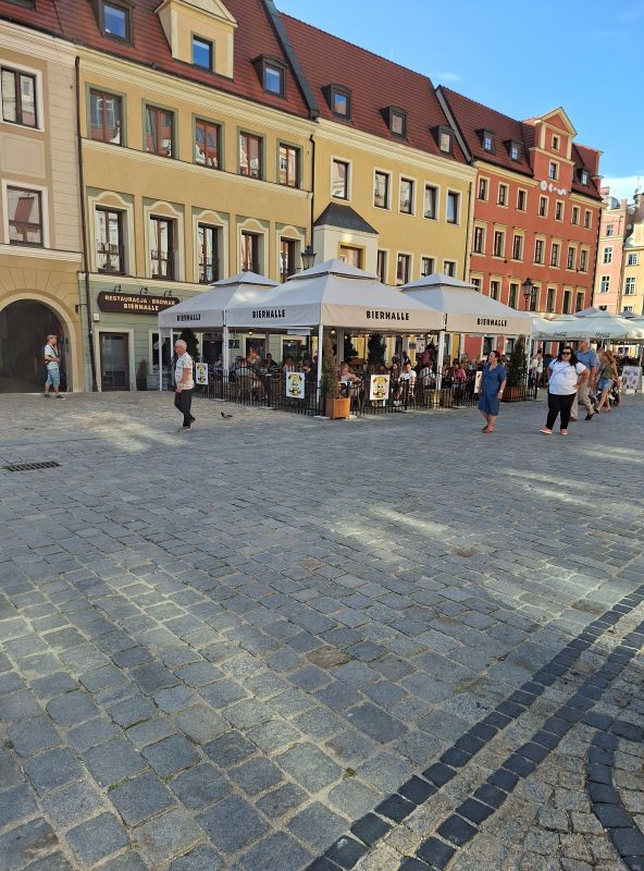 Außenbereich des Restaurants Bierhalle mit Tischen und Sonnenschirmen auf dem Kopfsteinpflaster des Breslauer Ryneks.