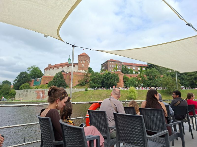 Fahrgäste auf einem Ausflugsschiff während einer Bootstour auf der Weichsel mit Blick auf die Burg Wawel im Hintergrund.