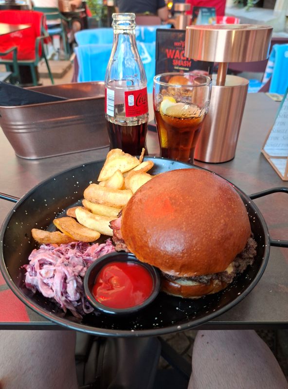 Servierter Burger mit Pommes frites, Krautsalat und eine Flasche Cola auf einem schwarzen Teller in einem Restaurant in Breslau.