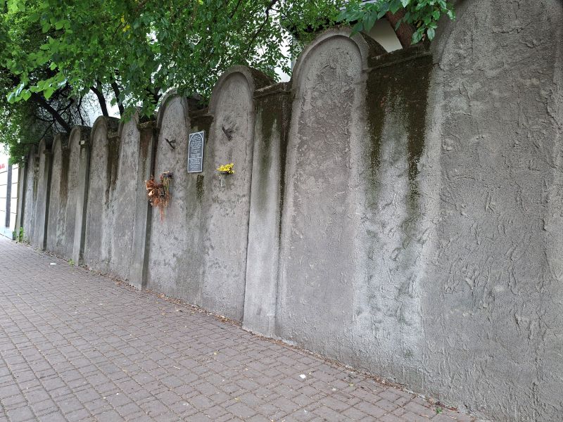 Nahaufnahme eines erhaltenen Teils der Krakauer Ghettomauer mit charakteristischen Rundbögen aus Stein.