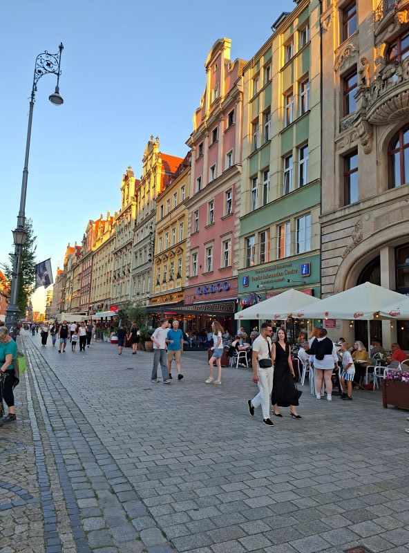 Belebte Fußgängerzone am Breslauer Rynek mit historischen Buntsandstein-Fassaden und Restaurant-Außenbereichen.