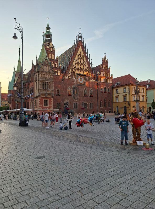 Das aufwendig verzierte alte Rathaus am Breslauer Ring bei sonnigem Wetter mit flanierenden Passanten.