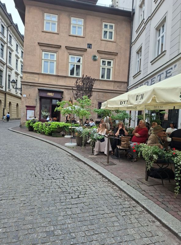 Gemütliches Straßencafé mit Sonnenschirmen und Gästen in den historischen Gassen der Krakauer Altstadt.
