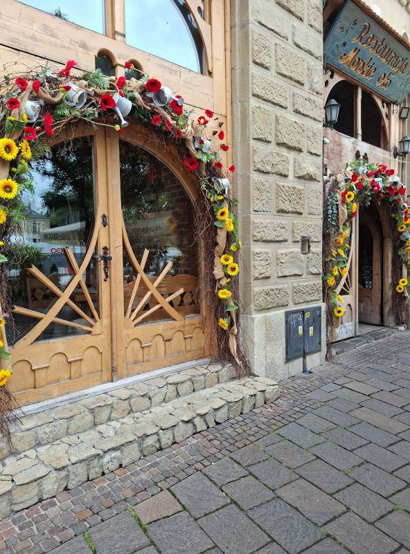 Holzverziertes Eingangsportal eines Restaurants in Krakau, dekoriert mit Blumengirlanden aus Sonnenblumen und Mohnblumen.
