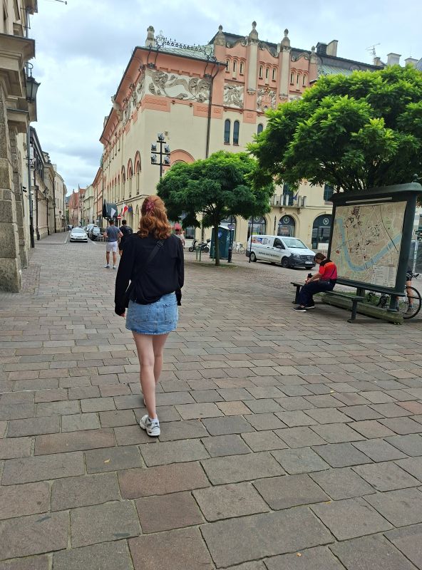 Partnerin des Blog-Autors spaziert über das Pflaster einer breiten Fußgängerzone in der Krakauer Altstadt vor einem historischen Gebäude.