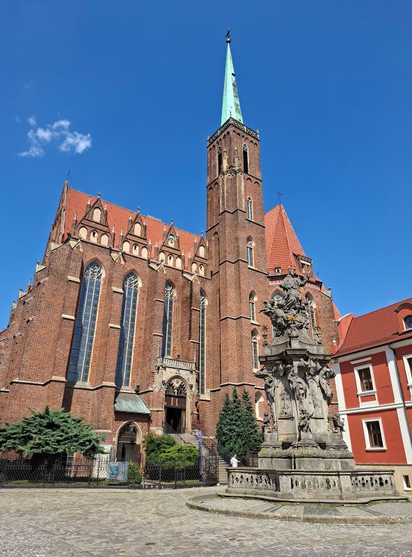 Die Stiftskirche zum Heiligen Kreuz und St. Bartholomäus in Breslau aus rotem Backstein vor strahlend blauem Himmel.