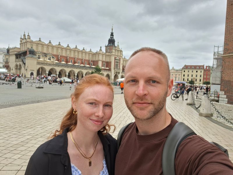 Selfie des Blog-Autor-Paares auf dem Krakauer Hauptmarkt mit den historischen Tuchhallen im Hintergrund.