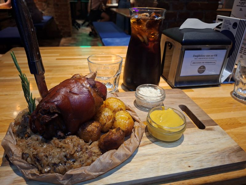 Deftige Schweinshaxe mit Röstkartoffeln, Sauerkraut, Senf und Meerrettich auf einem Holzteller im Restaurant Targowa Craft Beer und Food.