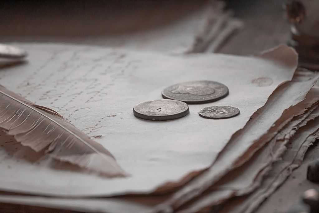 Aufnahme von antiken Münzen und einer Schreibfeder auf einem handgeschriebenen historischen Dokument. Ein Symbolbild für exponentielles Wachstum und historische Gedankenexperimente wie den Josephspfennig.
